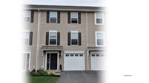 Exterior of townhouse with tan siding and dark brown shutters and front door