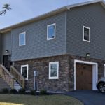 House with gray siding and stone siding. Stairs lead up to the front door and there are two garage doors on the side.