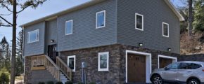 House with gray siding and stone siding. Stairs lead up to the front door and there are two garage doors on the side.
