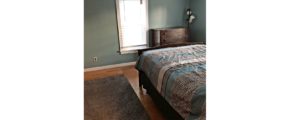 Bedroom with full bed, throw rug, wood dresser with four drawers, and a large window