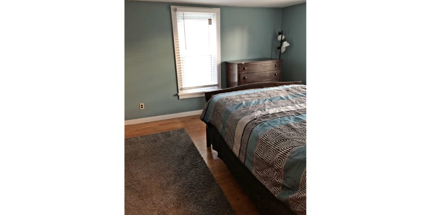 Bedroom with full bed, throw rug, wood dresser with four drawers, and a large window