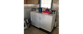 Laundry room with side-by-side top load washer and front load dryer with cabinets perpendicularly above.