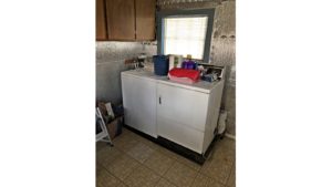 Laundry room with side-by-side top load washer and front load dryer with cabinets perpendicularly above.