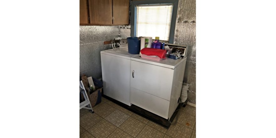 Laundry room with side-by-side top load washer and front load dryer with cabinets perpendicularly above.