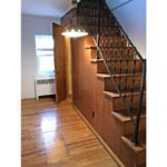 Wooden stair case with hanging light and hardwood floor.