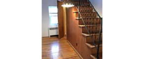 Wooden stair case with hanging light and hardwood floor.
