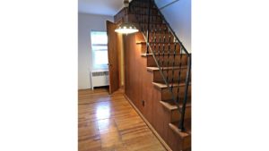 Wooden stair case with hanging light and hardwood floor.