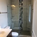 Bathroom with shower stall with frameless glass sliding door, toilet, and vanity with mirror