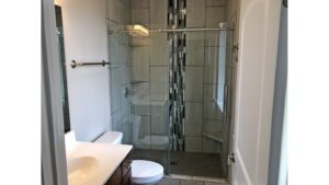 Bathroom with shower stall with frameless glass sliding door, toilet, and vanity with mirror
