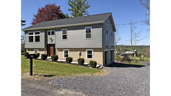 Exterior of house with gravel driveway, gray siding and yellow-painted brick.