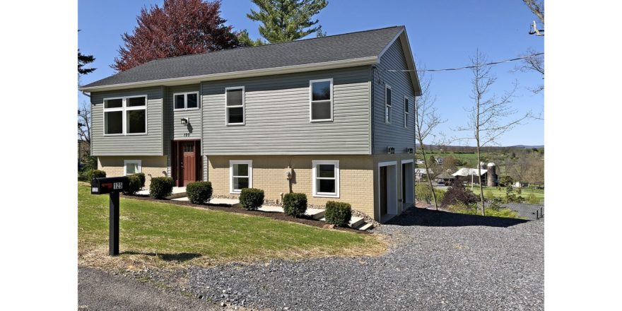 Exterior of house with gravel driveway, gray siding and yellow-painted brick.