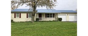 Exterior of ranch house with yellow siding and maroon shutters, covered front porch, two car garage, and tree