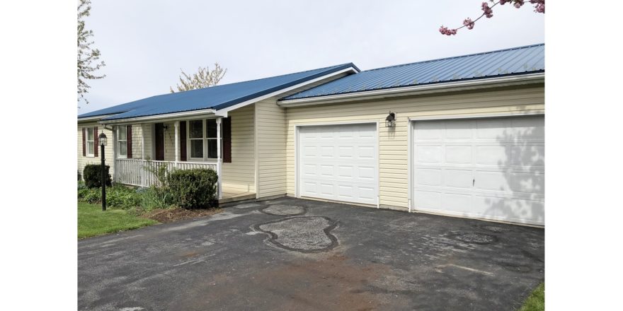 Exterior of ranch house with yellow siding and maroon shutters, covered front porch, two car garage, and driveway