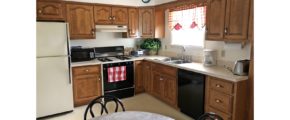 Kitchen with white and black appliances, wood cabinets, table with chairs and stool, and small window above the sink