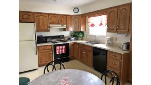 Kitchen with white and black appliances, wood cabinets, table with chairs and stool, and small window above the sink