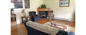 Living room with corner fireplace, pictures, couch and armchair, coffee table, end table, rocking chair, and bookcase
