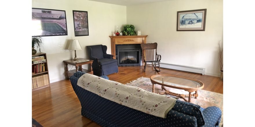 Living room with corner fireplace, pictures, couch and armchair, coffee table, end table, rocking chair, and bookcase