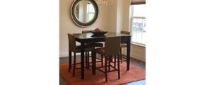 Dining room with square, bar-height dining table, wood-style flooring, accent rug, mirror, and window