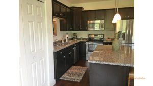 Kitchen with dark wood cabinets, wood-style flooring, stainless steel appliances, stone countertops, and island with bar seating