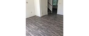 Unfurnished living room with gray, wood-style flooring and carpeted stairs to the second floor.