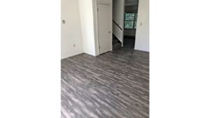 Unfurnished living room with gray, wood-style flooring and carpeted stairs to the second floor.