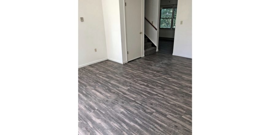 Unfurnished living room with gray, wood-style flooring and carpeted stairs to the second floor.