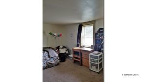 Carpeted bedroom with twin bed, lamp, window, desk and shelving