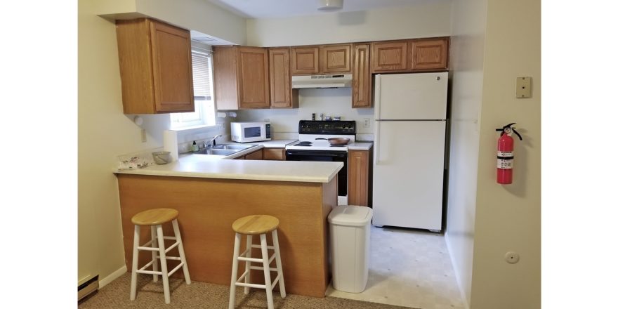 Kitchen with white appliances, wood-tone cabinets, and barstool seating