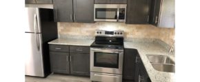 Kitchen with stainless steel appliances, dark gray cabinets, stone-style countertops, and wood-style flooring