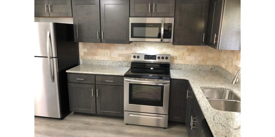 Kitchen with stainless steel appliances, dark gray cabinets, stone-style countertops, and wood-style flooring