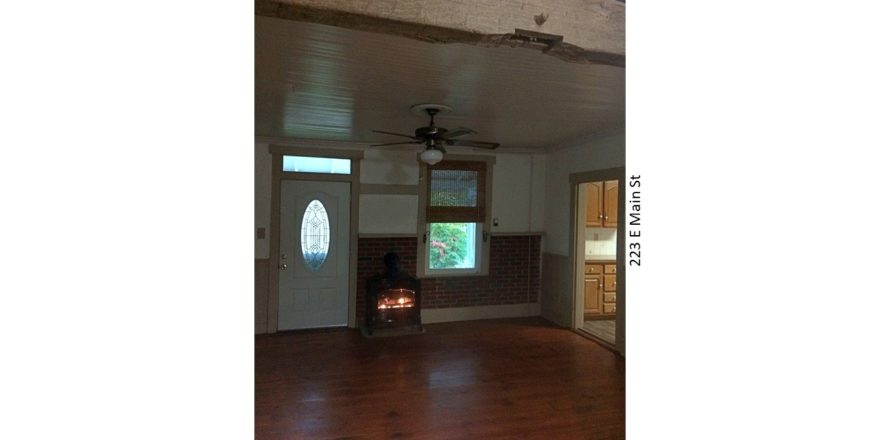 Living room with wood-burning fireplace, exposed brick, exposed beam, and hardwood floors