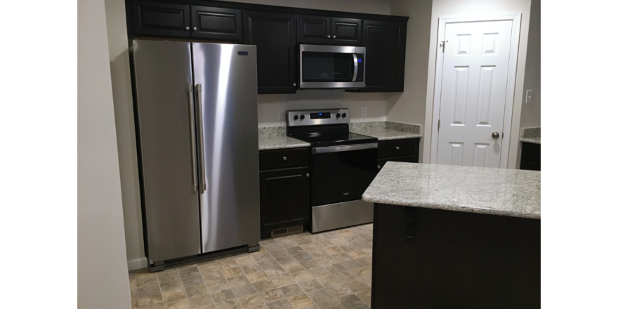 Kitchen with stainless steel appliances, black cabinets, and stone counter tops