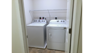 Laundry close with side-by-side top load washer and front load dryer with a white wire shelf above.