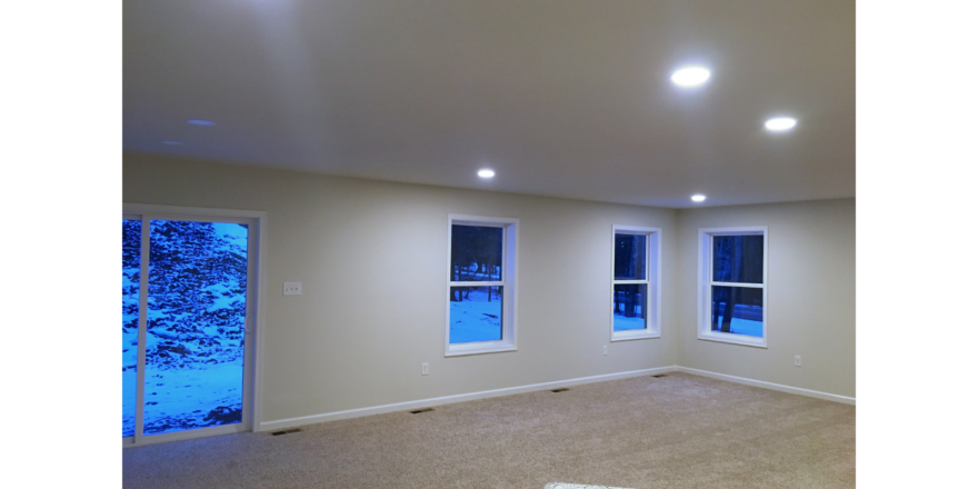 Unfurnished, carpeted living room with three windows and a sliding glass door.