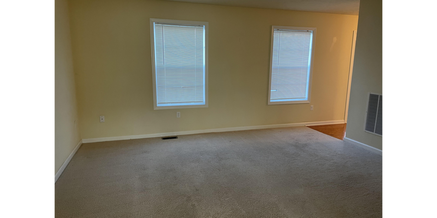 an empty room with two windows and carpet