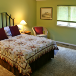 Bedroom with green walls, queen-sized bed, two end tables and a wicker chair