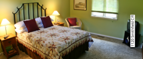 Bedroom with green walls, queen-sized bed, two end tables and a wicker chair