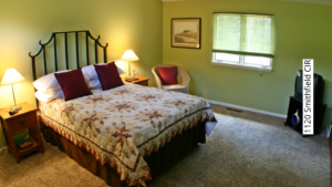 Bedroom with green walls, queen-sized bed, two end tables and a wicker chair