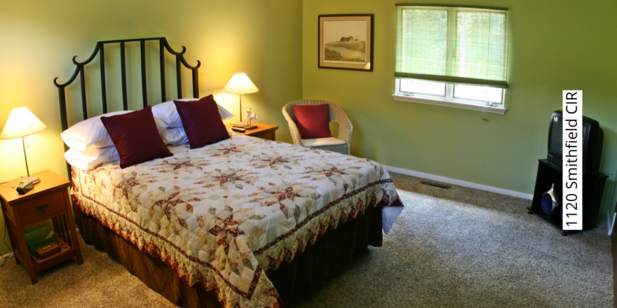 Bedroom with green walls, queen-sized bed, two end tables and a wicker chair