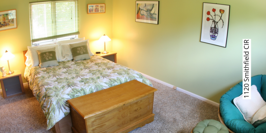 Bedroom with green walls, queen-sized bed, two end tables, and a lounge chair