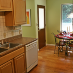 Kitchen with tan cabinets, white appliances, white tile backsplash, and small kitchen table