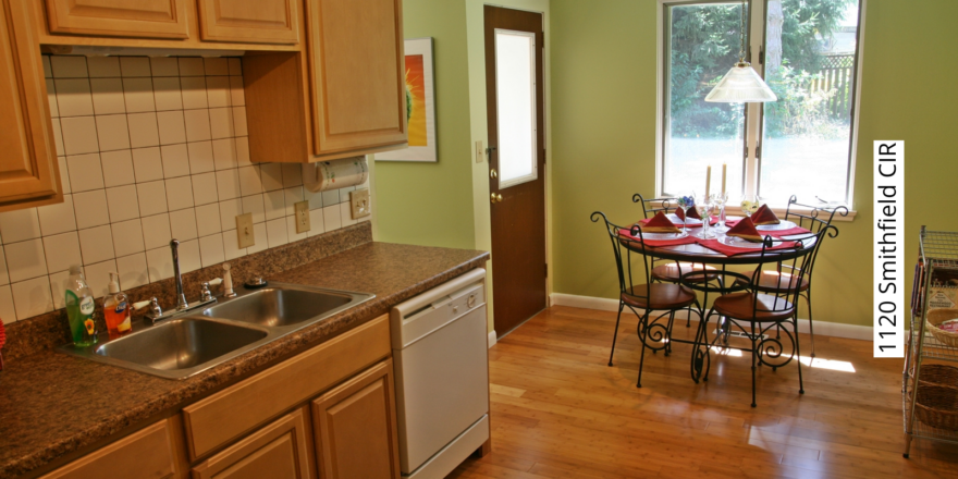 Kitchen with tan cabinets, white appliances, white tile backsplash, and small kitchen table