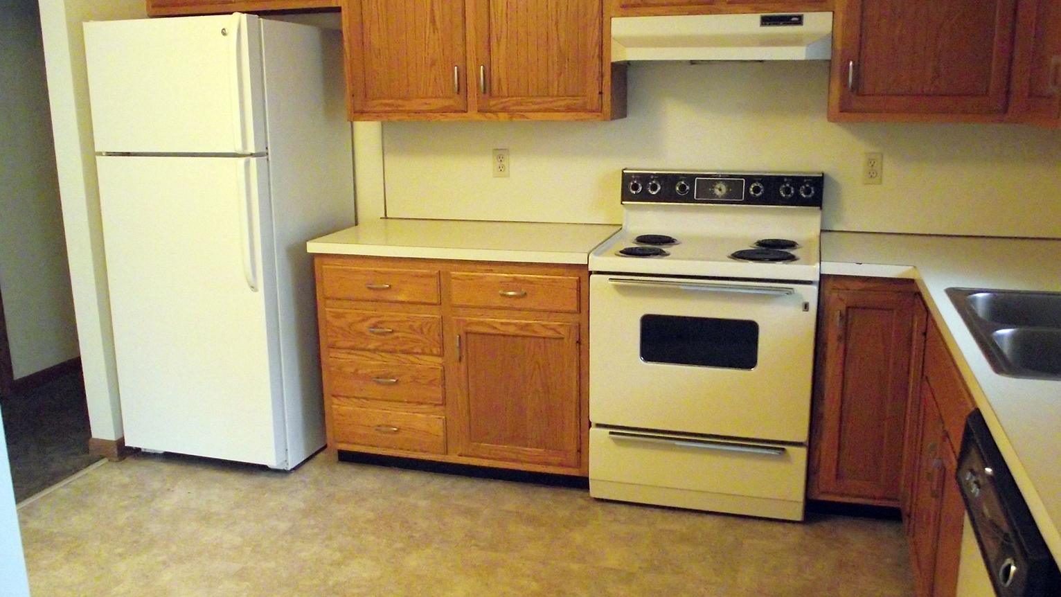 Empty kitchen with white fridge, stove, and wooden cabinets