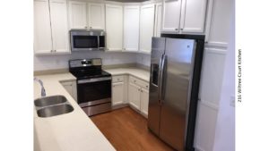 U-shaped kitfchen with white cabinets and countertops, hardwood floor, and stainless steel appliances