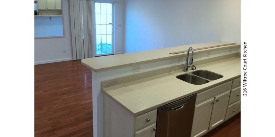 Kitchen with white countertops and cabinets, stainless steel dishwasher and sink and breakfast bar