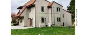 Rear exterior with patio and lawn. House has vertical, tan siding.