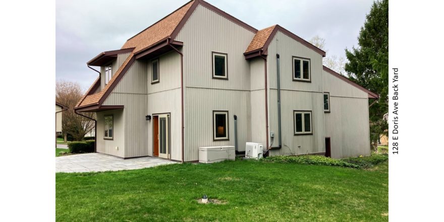 Rear exterior with patio and lawn. House has vertical, tan siding.