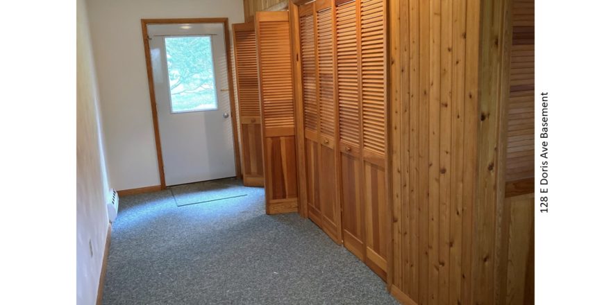 Carpeted basement with wood storage closets and exterior door.