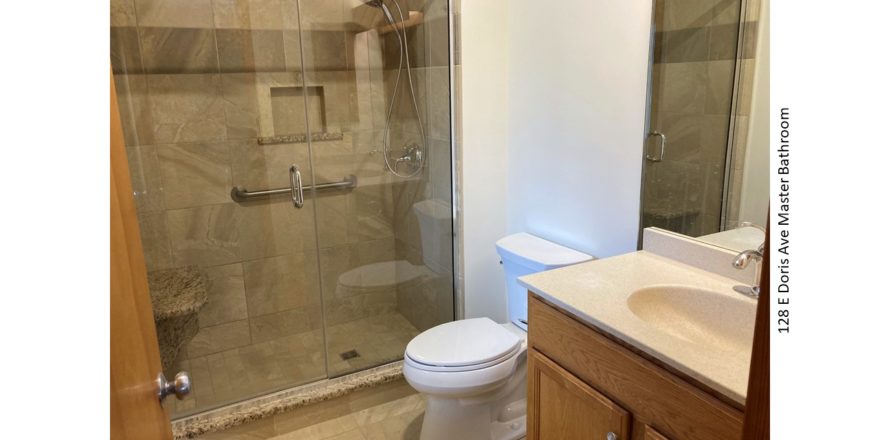 Bathroom with tile shower with glass door and seat, toilet, and vanity with mirror
