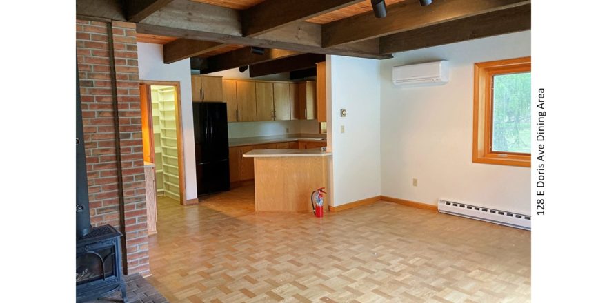 Dining area with wood-burning stove, light wood-style parkay flooring, fire extinguisher, and wood beams with track lighting